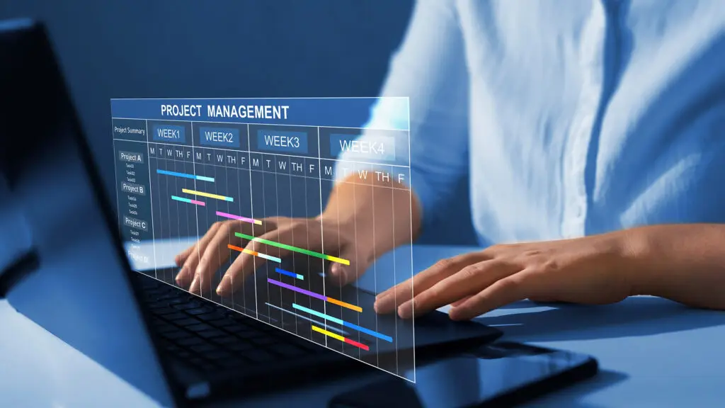 Person working on a laptop with a digital project management interface displayed in front. The screen shows a Gantt chart with tasks organized by projects and timelines over several weeks, emphasizing task progress and deadlines. The interface highlights modern project management tools and planning.