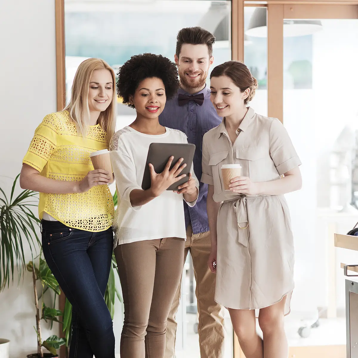 A group of four diverse people are gathered together, all smiling and engaged in what they are looking at on a tablet held by one of the women. The group seems to be in a casual office environment, with some of them holding coffee cups, which adds to the relaxed and collaborative atmosphere. This image represents the concept of "Your Rights and Responsibilities," indicating a positive and inclusive approach to understanding and respecting individual roles and duties within a community or organisation.